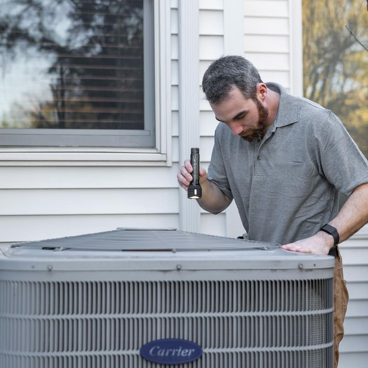 HVAC employee inspecting an outside condenser unit with flashlight